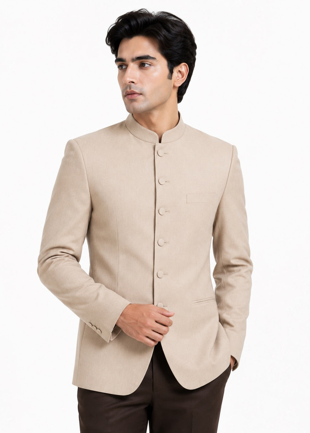 A man wearing a light beige mandarin collar Nehru jacket with buttoned front closure, paired with dark brown trousers, photographed against a plain white background.