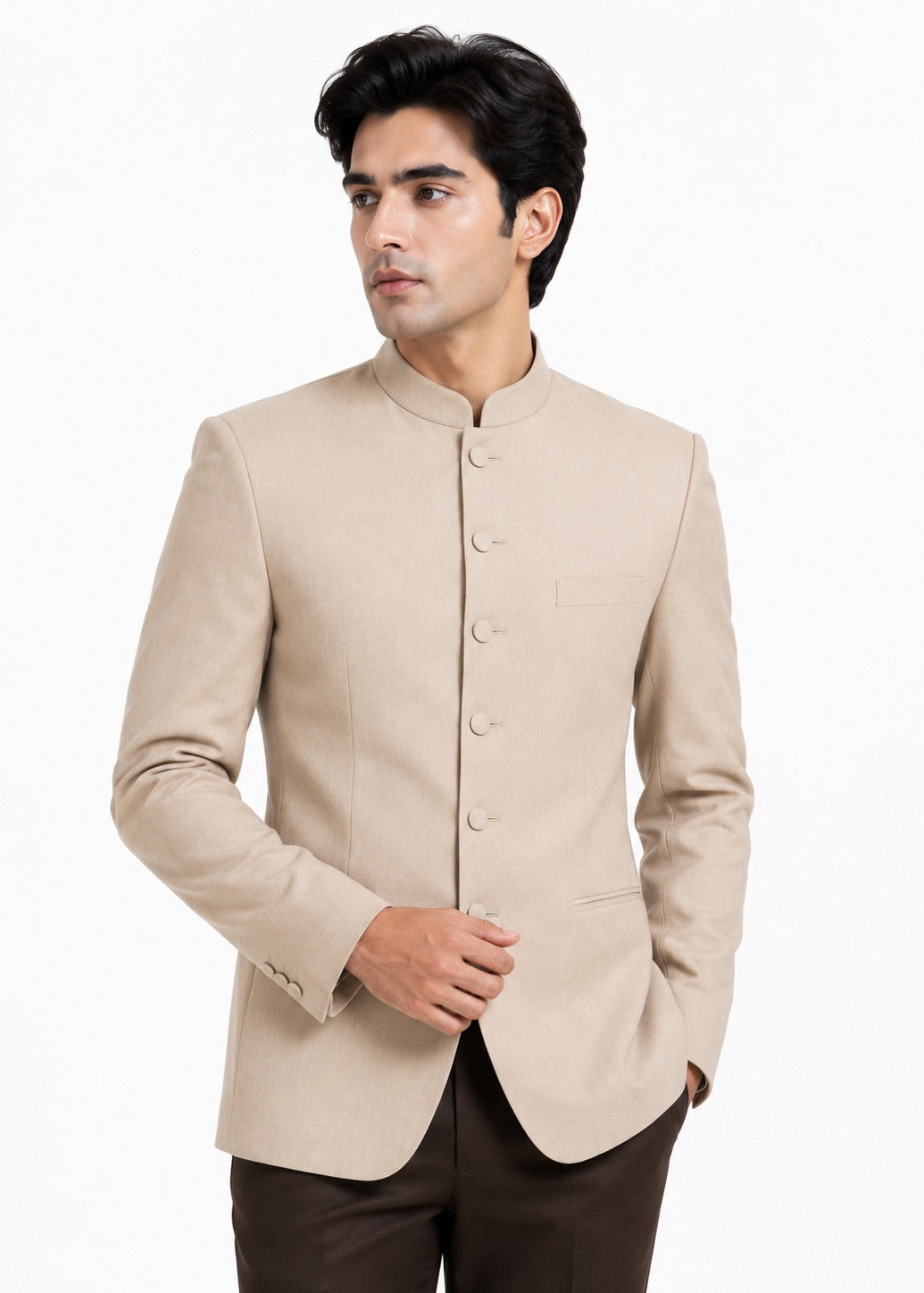 A man wearing a light beige mandarin collar Nehru jacket with buttoned front closure, paired with dark brown trousers, photographed against a plain white background.