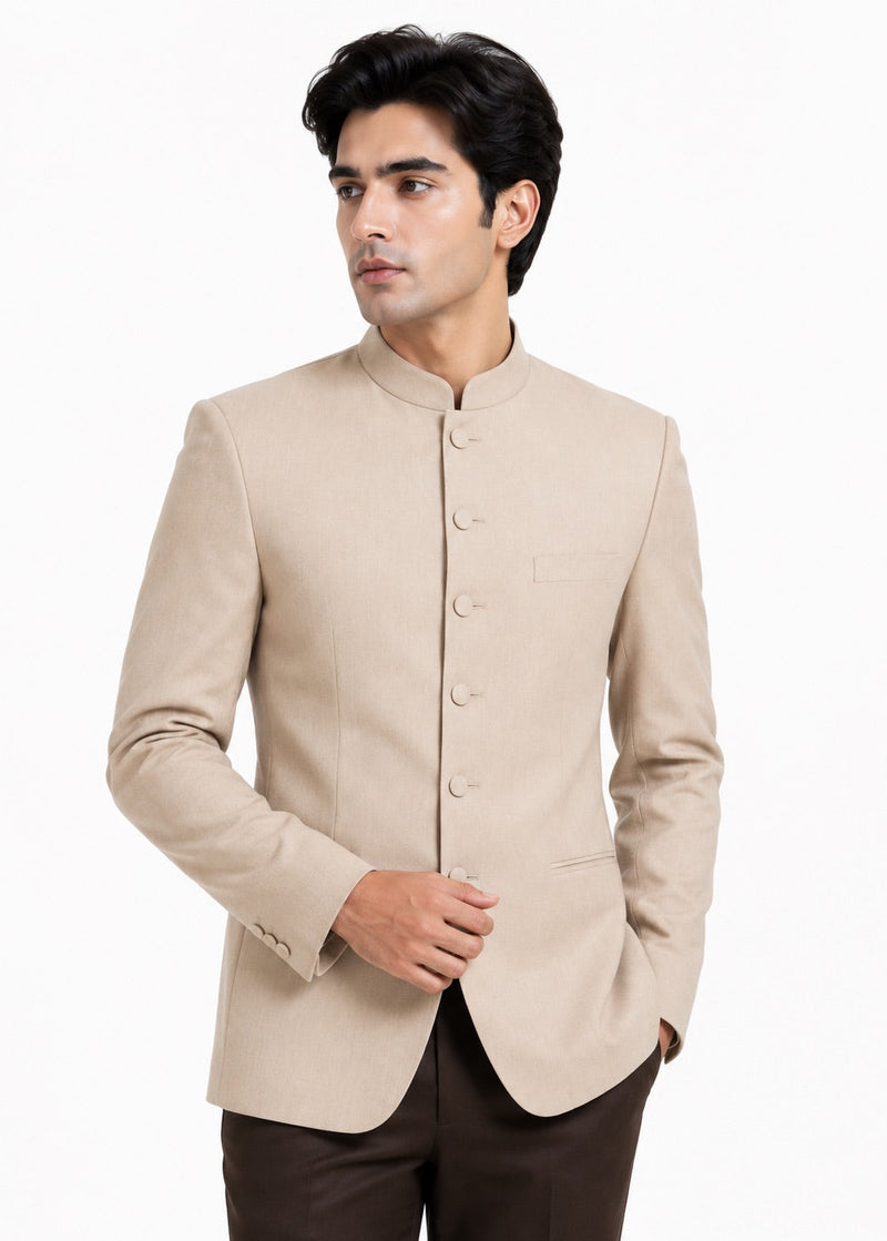 A man wearing a light beige mandarin collar Nehru jacket with buttoned front closure, paired with dark brown trousers, photographed against a plain white background.